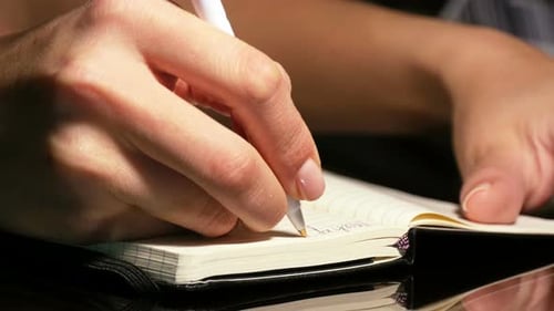 Woman writes in notebook with pen, close up