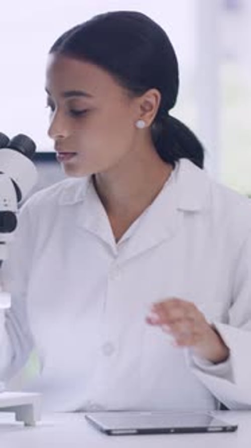 Woman Works with Microscope and Tablet in Lab