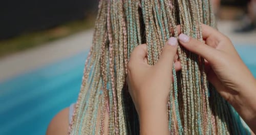 Una mujer admira las afrotrenzas de su hija las sostiene en la mano Vídeo de pie junto a la piscina