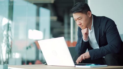 Business asian man in suit working on laptop computer in modern office coworking center. Confident