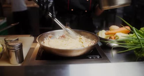 Close-up of a woman hand adding egg sauce/yolk mixture with cheese on spaghetti