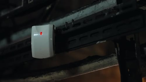 Closeup of a Mounted Security Sensor with Bright LED Indicators on a Metal Support Rail Above