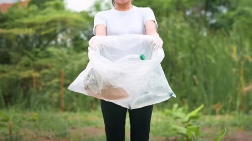 Woman Holding Bag of Trash in Green Landscape