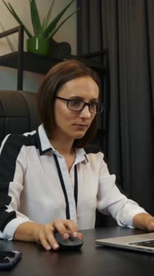 Confident, focused woman in glasses working on laptop in office. Vertical video