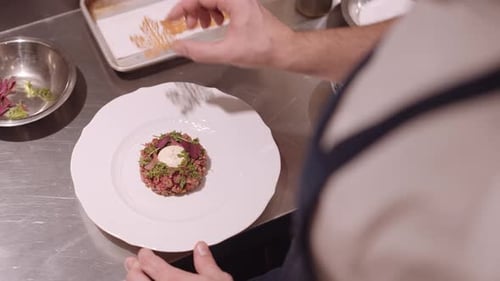 Male cook put decoration on the white plate with appetizer and pass the plate to be served. Close up