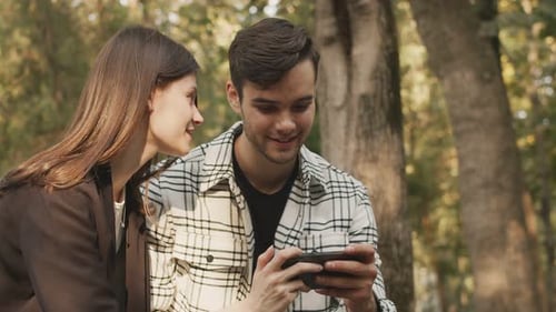 Girlfriend and Boyfriend Watching Video on a Mobile Handheld Device While Talking Green Trees Nature