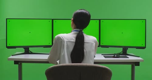 Asian Woman Thinking While Working With Mock Up Multiple Computer Monitor In Green Screen Studio