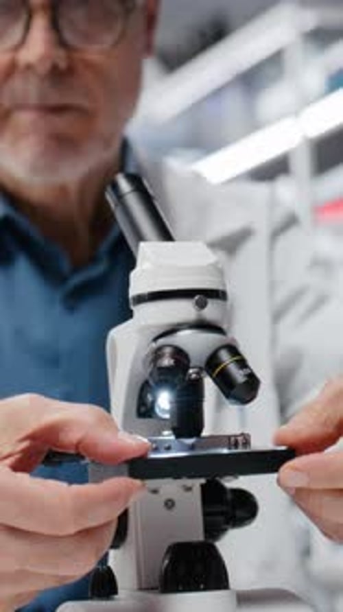 Senior Man Adjusting Slide Under Microscope in Lab