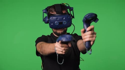 A Man Uses Virtual Reality Glasses to Play in a Studio on a Green Background