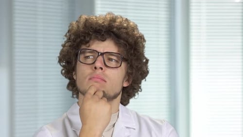 Close Up Portrait of a Pensive Young Doctor or Scientist in Glasses Thinking Indoors