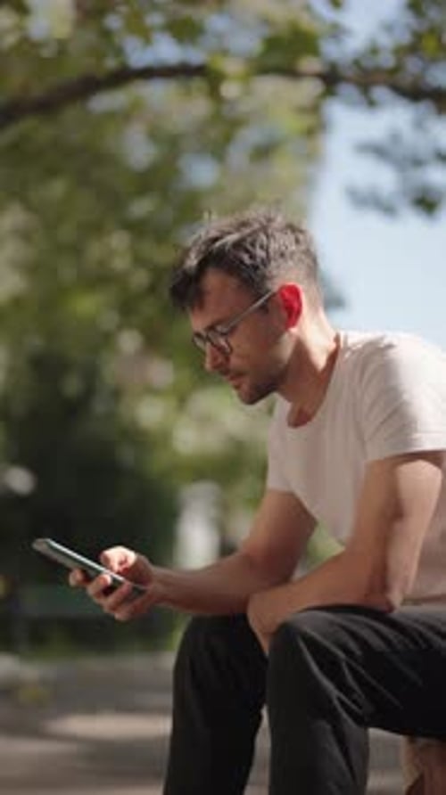 Man Using Smartphone on Park Bench on Sunny Summer Day