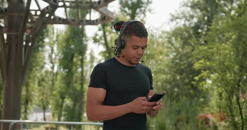 Man Listens with Headphones Using Phone in Park