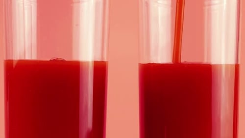 Le jus de tomate est versé dans des gobelets en verre sur fond rose. Ralenti.
