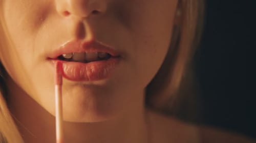Belle jeune femme applique du rouge à lèvres rouge sur ses lèvres sur fond noir