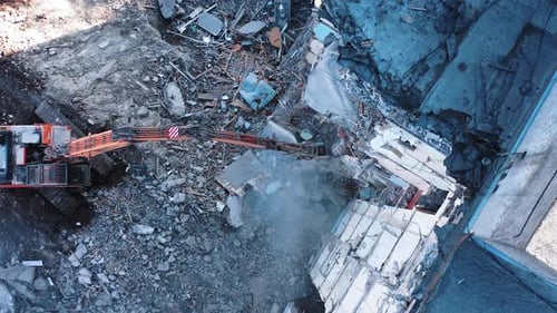 Long claw of an excavator destroys the concrete parts of the building.