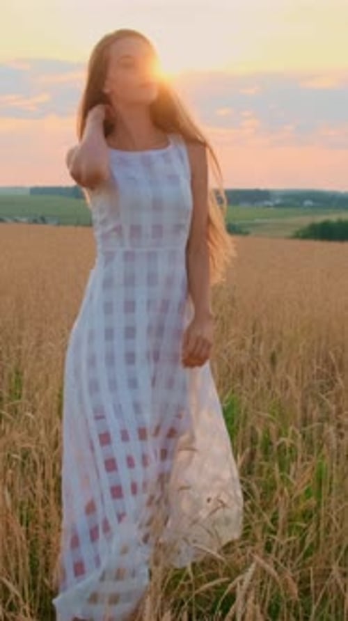 Young Woman in Flowing White Dress Dancing in Golden Wheat Field During Sunset with Vibrant Sky