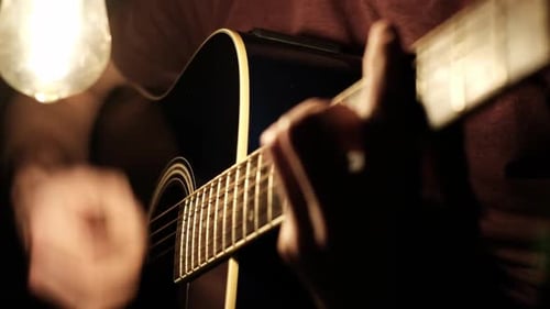 Man Plays Guitar Under Warm Lamp Close Up