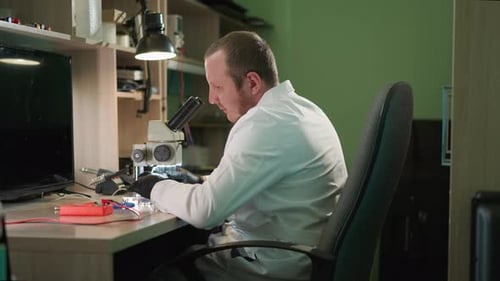 Man Looks Through Microscope in Workplace