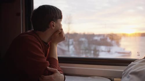 Un homme attentionné prend le train et regarde par la fenêtre au coucher du soleil