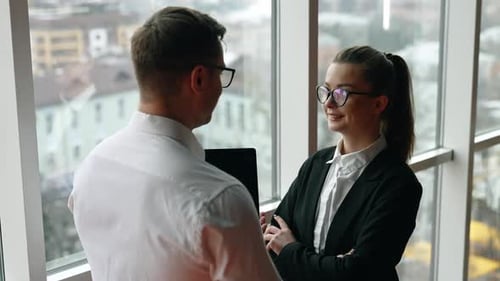 Diverse gender colleagues stand at the window communicating.