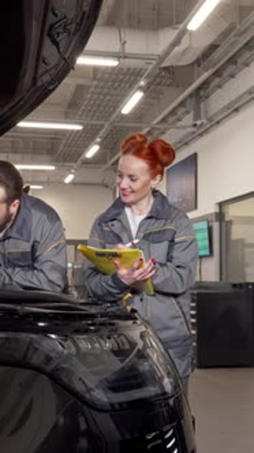 Dedicated Car Mechanics Inspecting Engine While Taking Notes