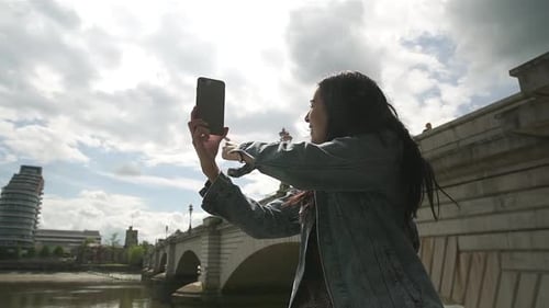 Hispanic Latina tourist using Skype and showing her friend the river Thames and Putney Bridge in Lon