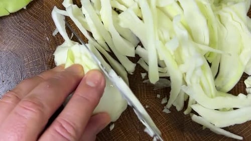 Ein Koch schneidet Kohl mit einem Messer auf einem Holzschneidebrett.