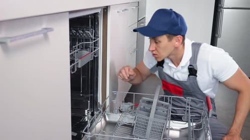 Männlicher Klempner inspiziert das zu reparierende Spülmaschinenteil in der Küche