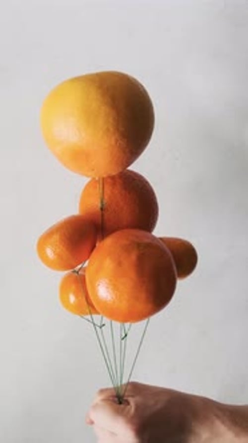 Hand Holding Fruit Balloons on White Background
