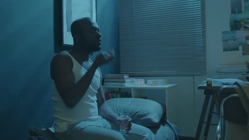 Man Taking Medicine in Dark Bedroom at Night