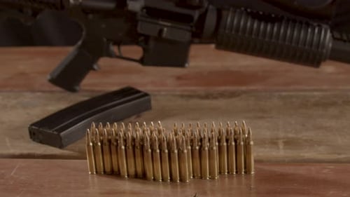 Dolly out of 5.56 ammunition with an AR-15 rifle with a scope in the background