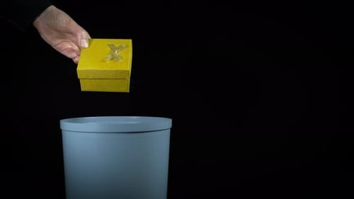 Hand Discards Yellow Gift Box in Trash Can