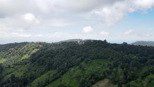 Aerial drone forward moving shot of a Buddhist temple in ditance over the hill top between green tre