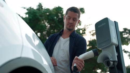 Man recharging battery for electric car during road trip. Exalt