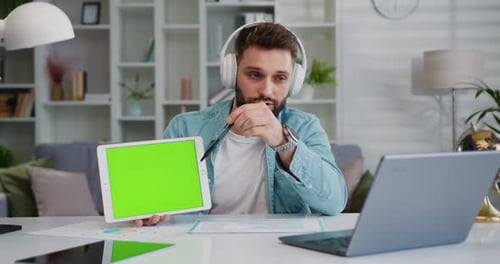Hombre de negocios concentrado sentado en el escritorio hace una videollamada, conferencia, discurso y muestra una pantalla verde digital