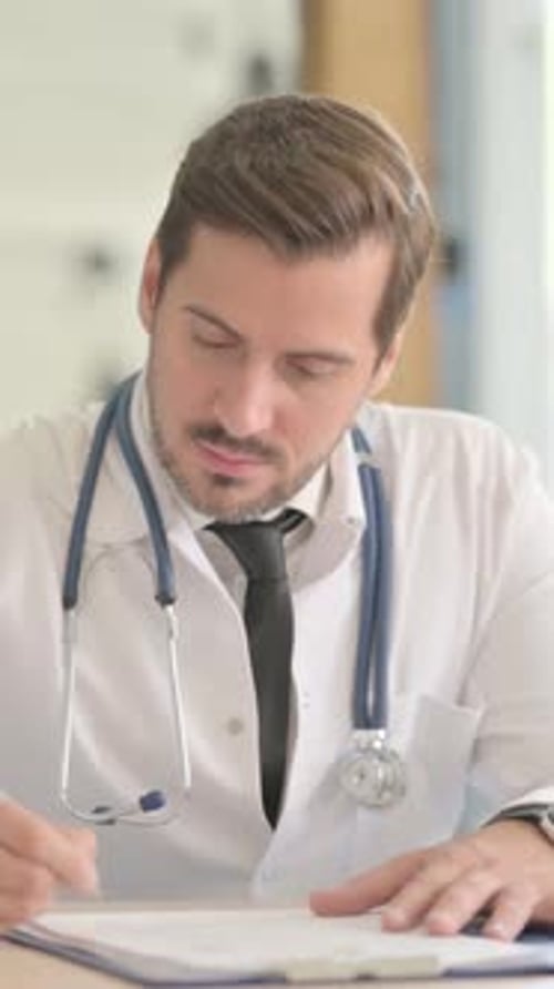 Male Doctor Working on Medical Report in Clinic, vertical video