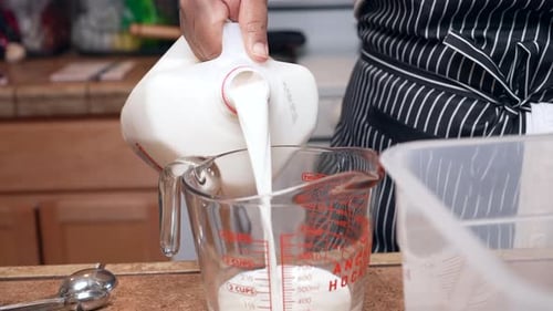 Pouring whole organic milk into a measuring cup for a special, homemade recipe - side view