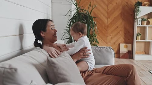 Mama sitzt auf dem Sofa und Baby springt vor Aufregung