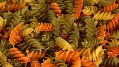Multicolored italian pasta Rotini or Fusilli rotating background closeup side view low light