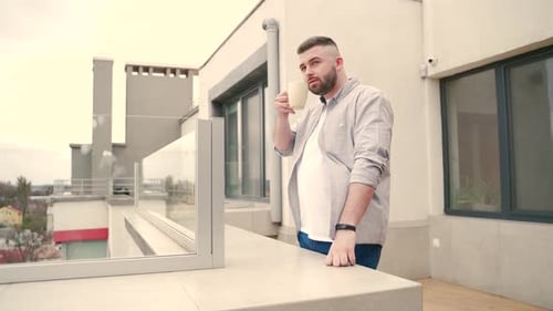 young handsome bearded man standing on modern balcony or terrace enjoying city view on urban