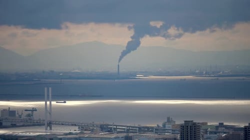 Blick auf die Skyline der Stadt am Meer mit Industriekamin und moderner Brücke