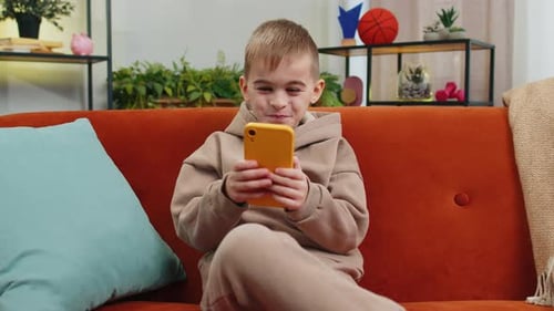 Boy in Sweatsuit Using Phone on Couch