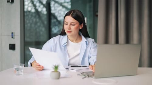 Femme concentrée travaillant sur un ordinateur portable examinant des documents au bureau