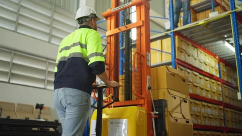 Warehouse worker man stand to control cargo truck during his coworker carry box out from cargo truck