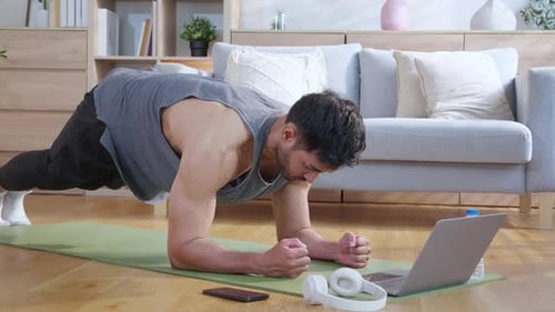 Man Does Plank Exercise Near Laptop at Home