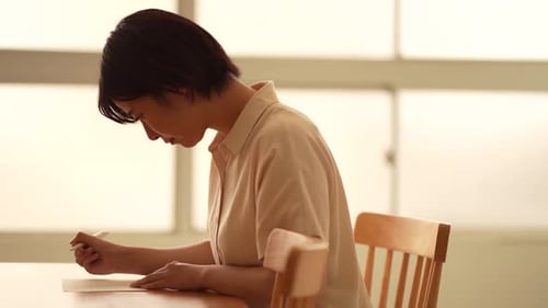Woman Sitting at Table Writing on Paper Indoors