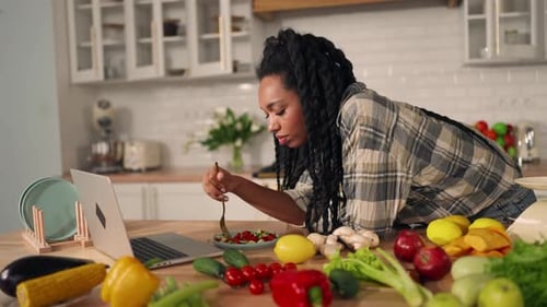 Woman with Laptop Eats Salad in Bright Kitchen