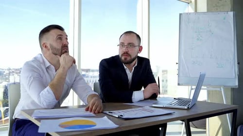Businessmen Discussing Financial Charts in Bright Office
