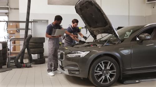 Two Auto Mechanics Inspecting Car Engine in Workshop