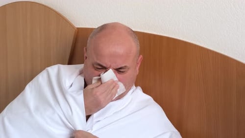 Homme malade assis sur son lit à la maison et se mouchant